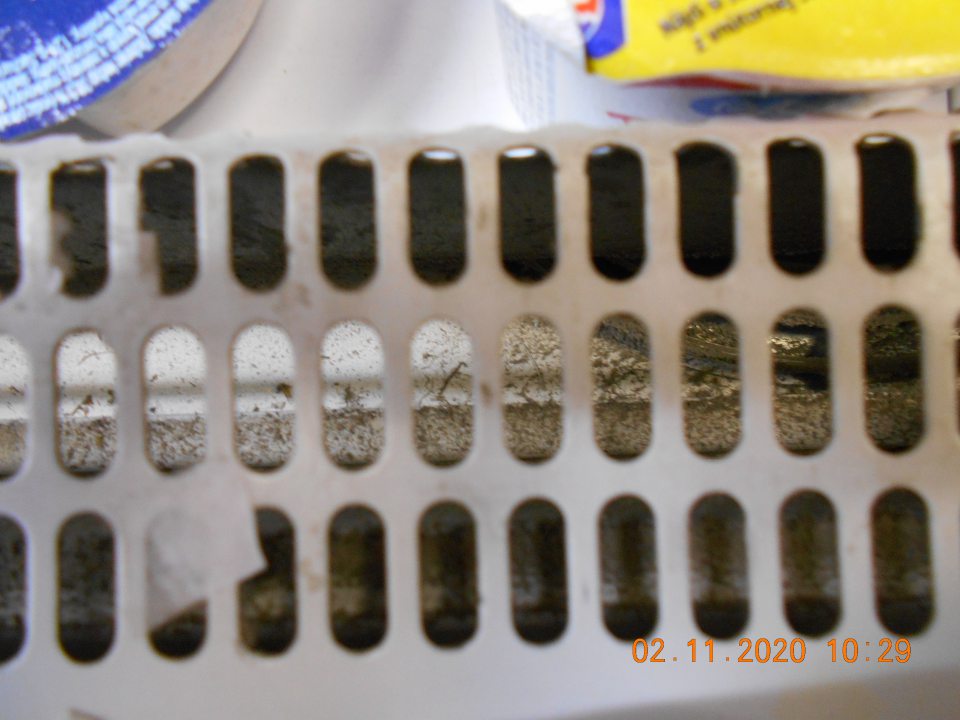 Znečistený priestor pod mriežkou v chladiarenskom zariadení s uchovávanými mliečnymi výrobkami na predajnej ploche.