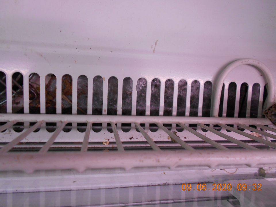 Zistené znečistené dno chladiarenského zariadenia s uchovávanými mliečnymi výrobkami na predajnej ploche.