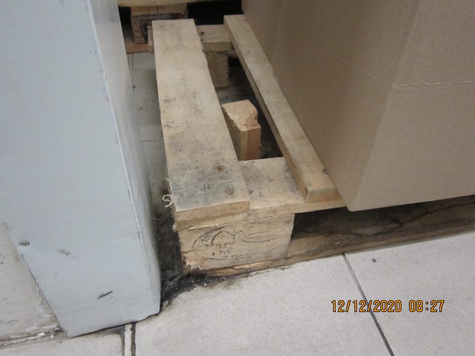 Znečistená podlaha na predajnej ploche pri palete s alkoholickými nápojmi – prach, pavučina, zaschnutá čierna špina.