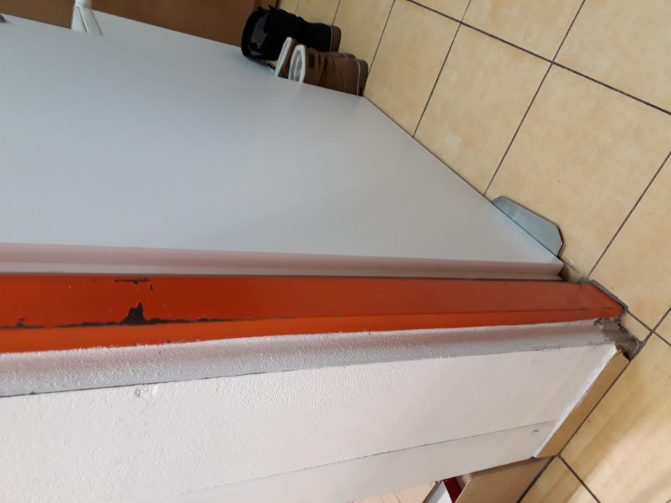 V zázemí predajne, porušená celistvosť obkladu v spodnej časti pri vstupe do dvier kancelárie, porušená celistvosť náteru zárubne pri vstupe do kancelárie.