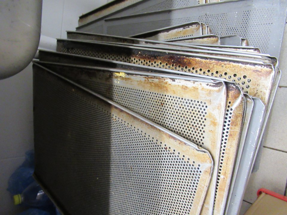 Plechy na pečenie znečistené zapečenou mastnotou a zbytkami po pečive.