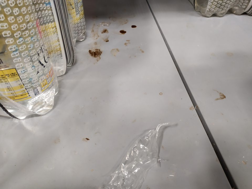 Znečistený regál na predajnej ploche zaschnutým obsahom potravín a zvyškami obalového materiálu.