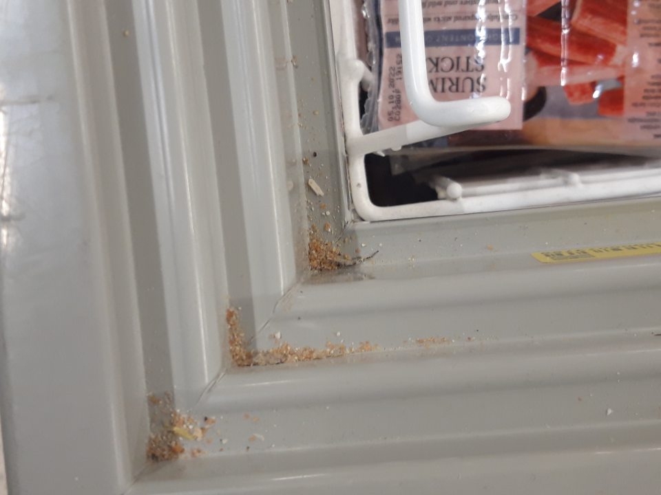 Obvodové drážky posuvných dvierok znečistené prachom, omrvinkami a zbytkami obalového materiálu a drobnými nečistotami.