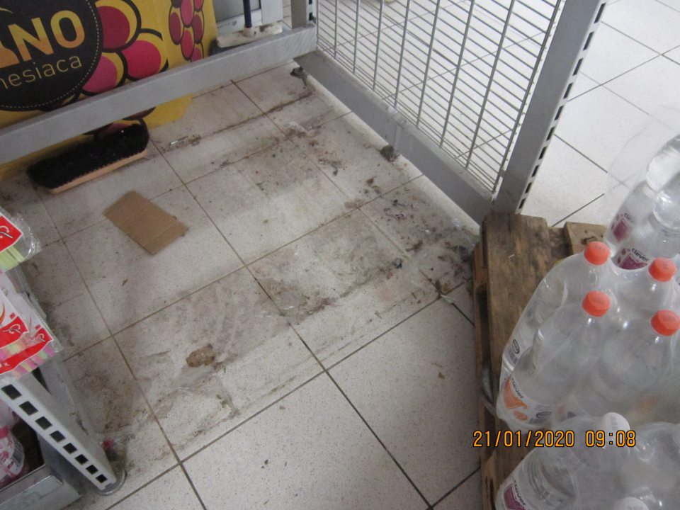 Na predajnej ploche znečistená podlaha prachom, napadanými nečistotami pod paletou s nápojmi.