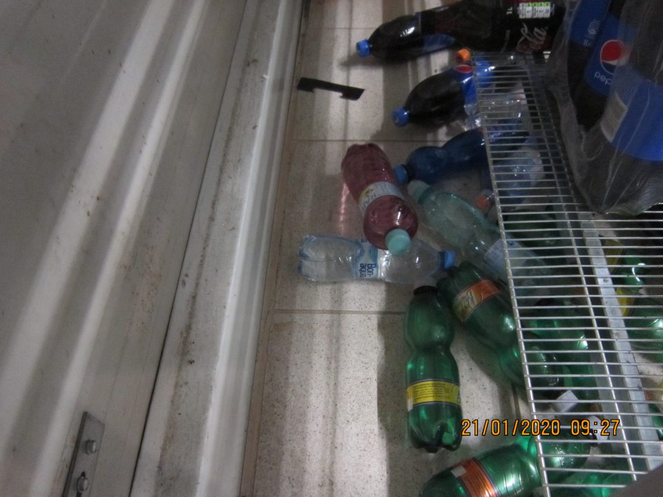 Na predajnej ploche za regálom s nápojmi popadané fľaše s nápojmi, nečistoty na podlahe.