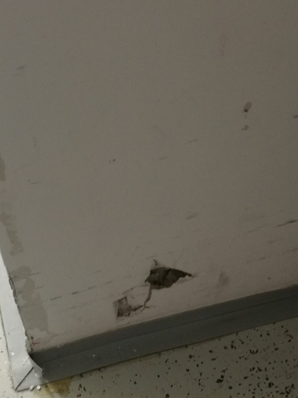 Diera v sadrokartónovej stene v spodnej časti oproti kancelárii, opadaný stavebný materiál