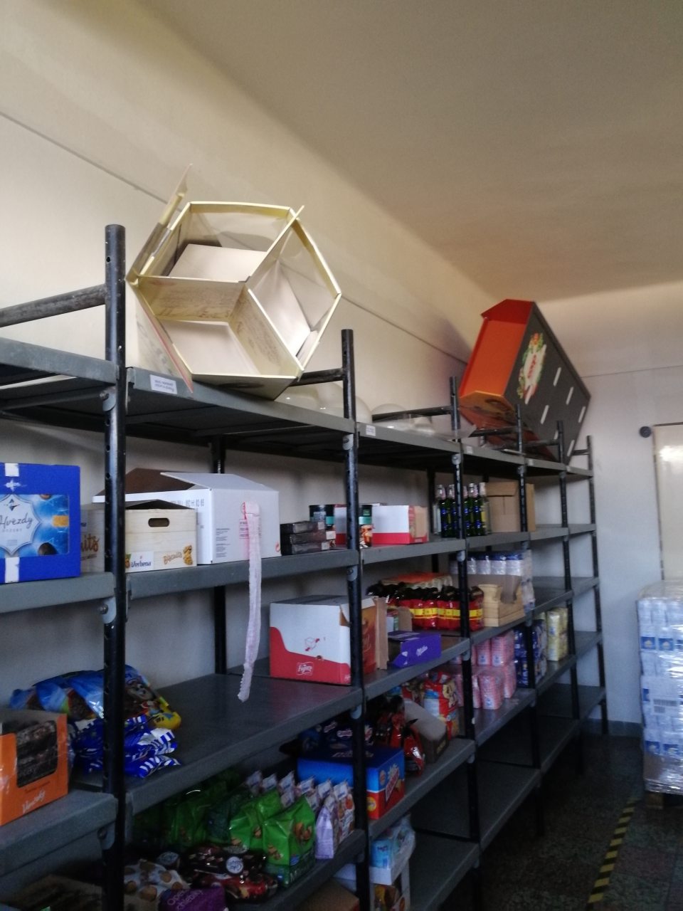 V priestoroch skladu sú potraviny, rôzne predmety, kartóny uložené chaoticky a neusporiadane.