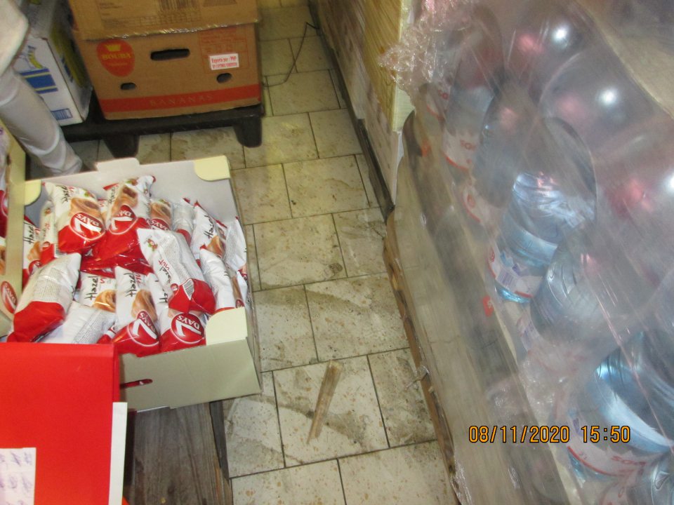 Znečistená podlaha v zázemí prevádzky pri paletách s trvanlivým pečivom výskyt nánosov prachu, kúskov z paliet a nečistôt.