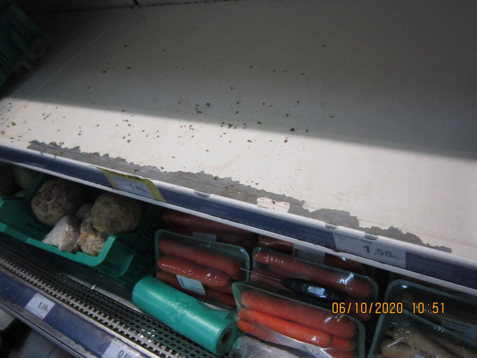 Regál chladiaceho zariadenia s uloženými uhorkami a kivi znečistený nánosom nečistôt a tiež zistený olupujúci sa povrchový hygienický náter na viacerých miestach o rozmeroch cca 60 cm x 2 cm, 8 cm x 1 cm Bočná stena chladiaceho zariadenia - sklenená výplň v spodnej časti na ľavej strane znečistená starším nánosom nečistôt V spodnej časti chladiaceho zariadenia s uloženou zeleninou zistený nános nečistôt pod kovovou mriežkou aj okolo kovovej mriežky Predné bočné steny chladiaceho zariadenie poškodené, na pravej strane poškodený povrch s vylomenými časťami na troch miestach o rozmeroch cca 5cm x 1cm, 2cm x 1cm a 1cm x 1 cm a na ľavej strane vylomené povrchové časti na dvoch miestach o rozmeroch cca 1cm x 0,5cm a 2cm x 0,5 cm