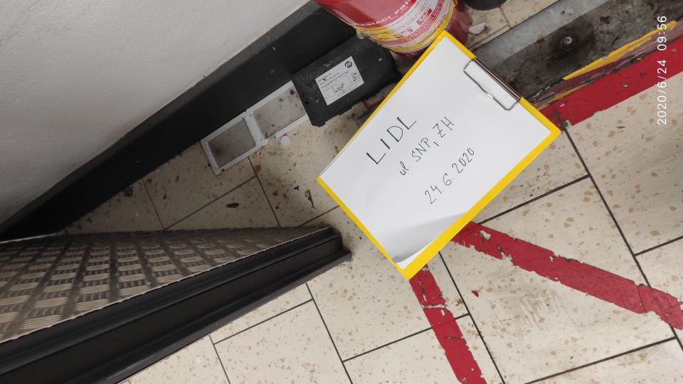 Znečistená podlaha zvyškami potravín a prachom pri východe zo skladu na predajnú plochu.