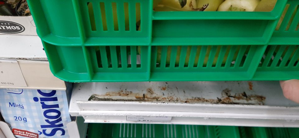 Znečistené kovové regále v predajni, na ktorých sú umiestnené plastové prepravky so zeleninou a ovocím prachom a zaschnutými zvyškami od zeleniny.