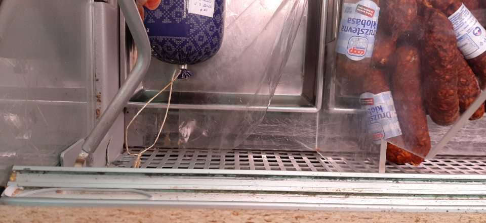 Znečistená chladiaca vitrína na uchovávanie mäsových výrobkov v predajni zbytkami potravín v ložnej časti a v drážkach posuvných dverí.