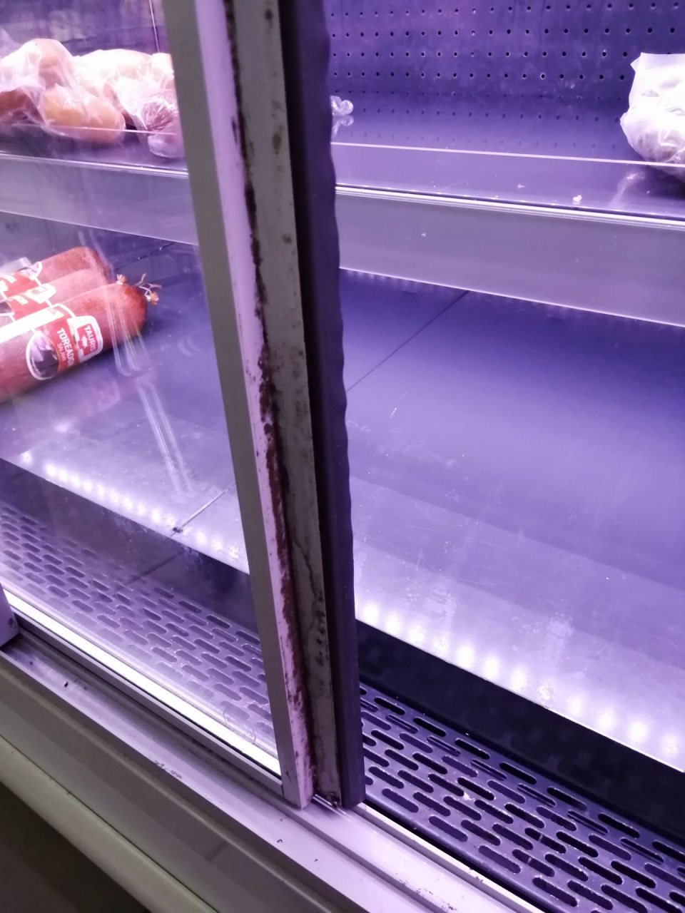 Znečistené predné lišty dvierok chladiacej vitríny s vystavovanými mäsovými výrobkami.