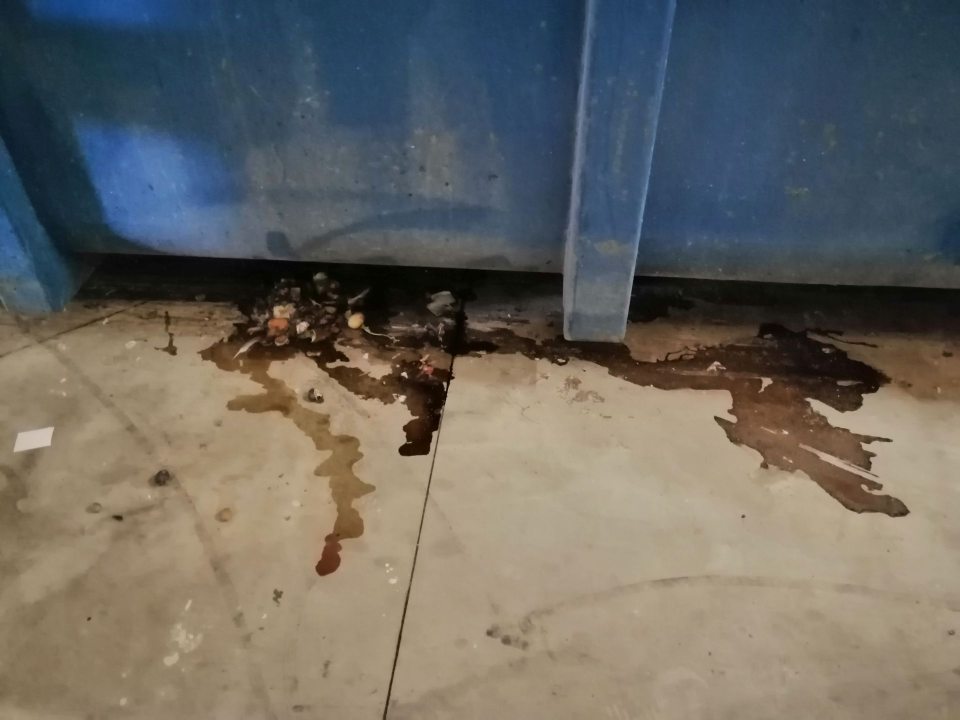 Zatečená a znečistená podlaha pod veľkokapacitným kontajnerom vo vonkajšom priestore príjmu potravín.