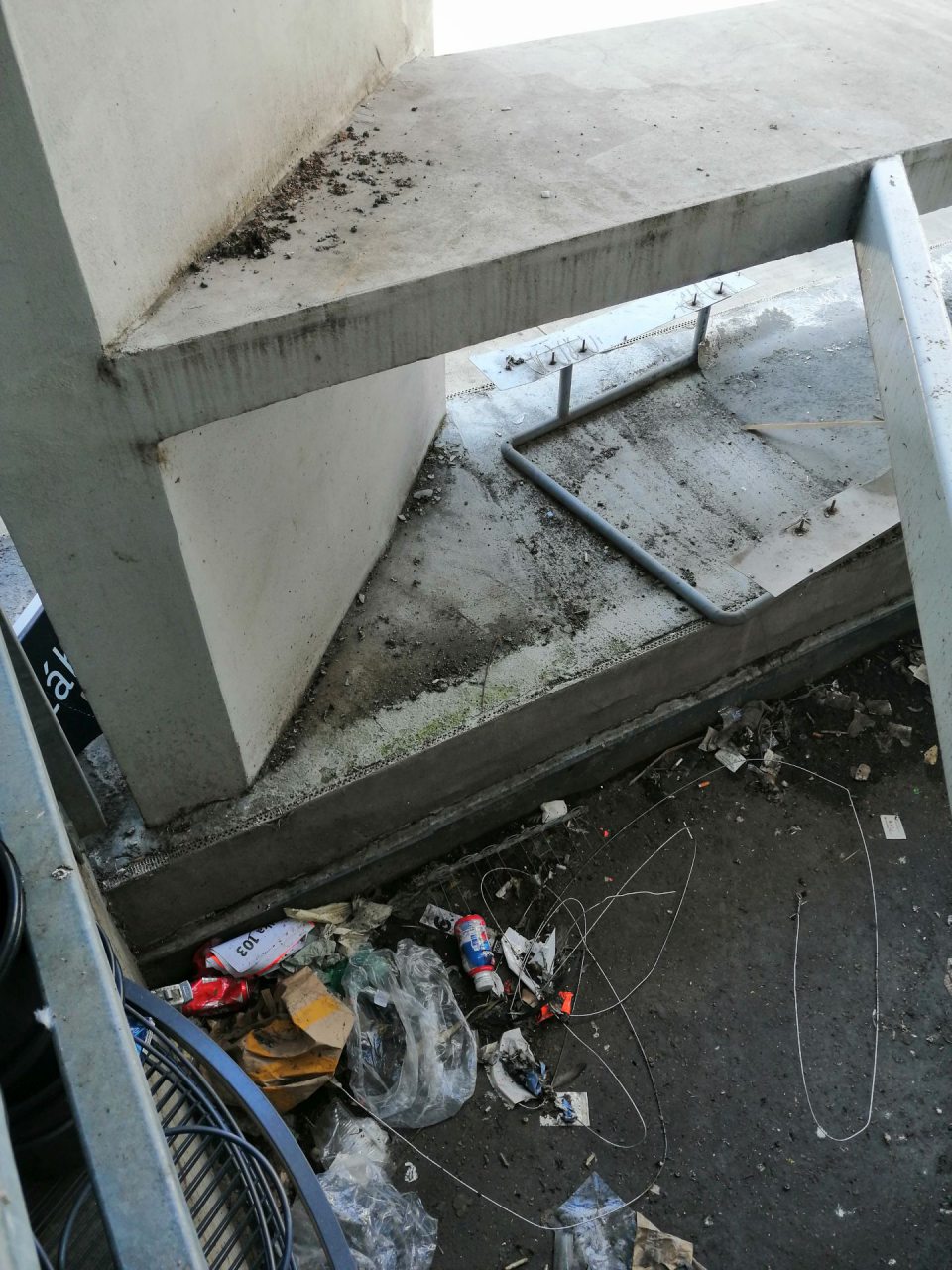 Výrazný nános nečistôt a odpadkov pod rampou vo vonkajšom priestore príjmu potravín.