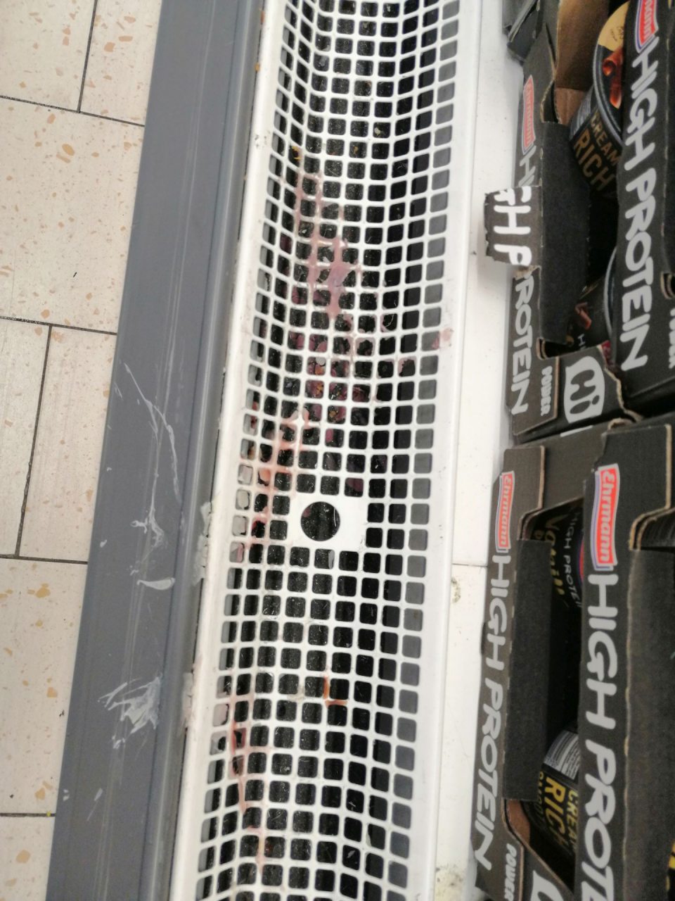 Znečistená mriežka a priestor pod mriežkou chladiaceho zariadenia s mliečnymi výrobkami.