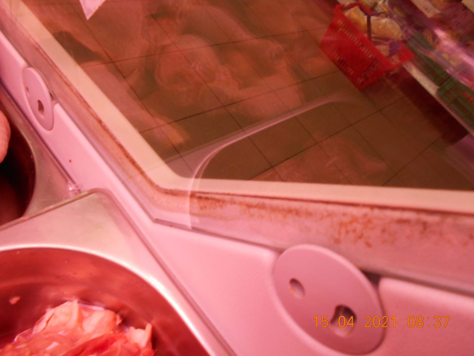 Zistená znečistená chladiarenská vitrína v ťažko dostupných miestach- medzi sklom a kovovou konštrukciou, s uchovávanými mäsovými výrobkami, na predajnej ploche.