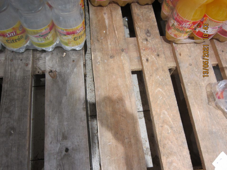 Znečistená podlaha pod paletami s uloženými nealkoholickými nápojmi na predajnej ploche- prach, nánosy zaschnutej špiny.