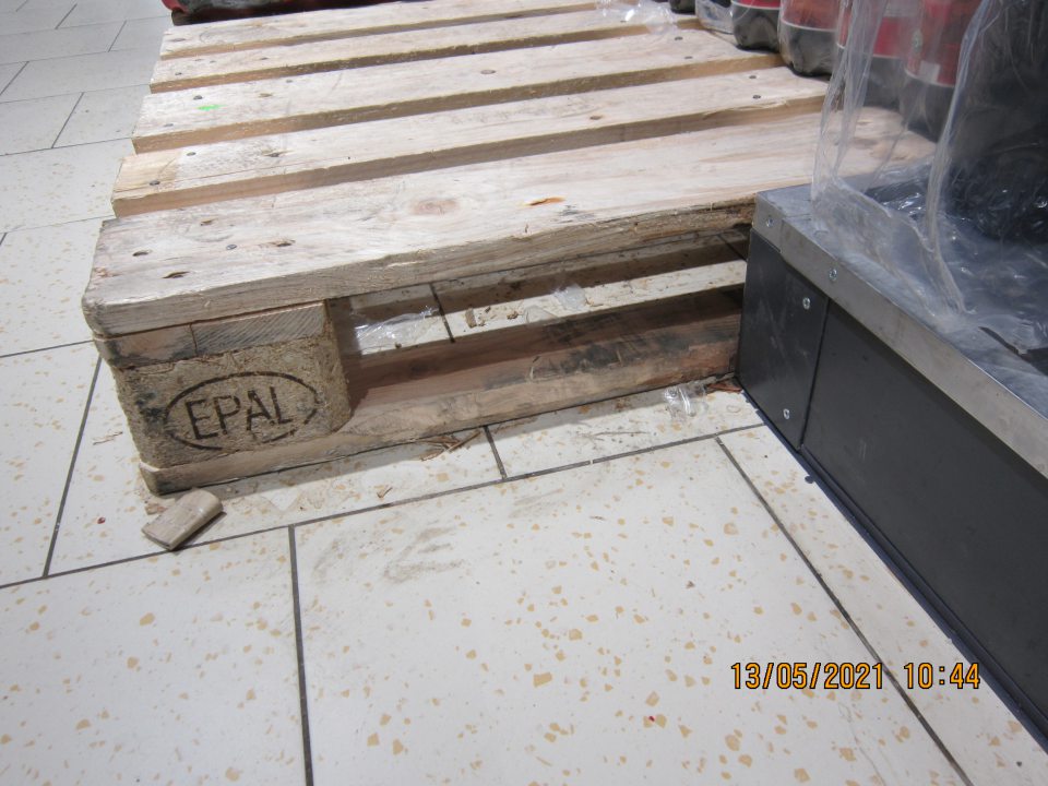 Znečistená podlaha pod paletami s uloženými nealkoholickými nápojmi na predajnej ploche- prach, zbytky obalového materiálu, triesky, nánosy zaschnutej špiny.