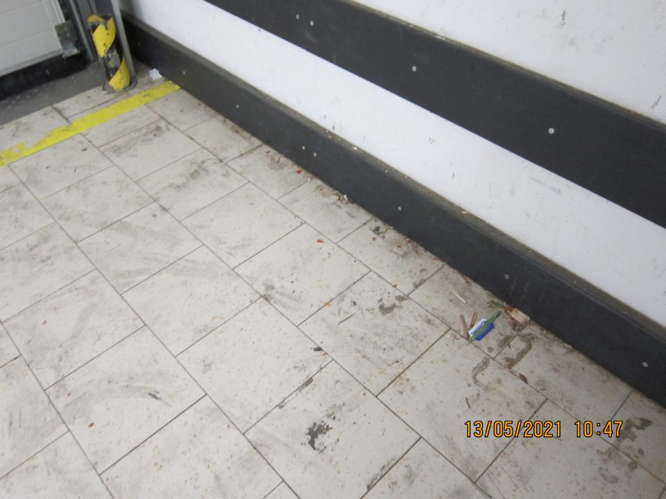 Znečistená podlaha v skladovacích priestoroch pri rampe- prach, nánosy zaschnutej čiernej špiny, drevené úlomky, kúsky papiera.