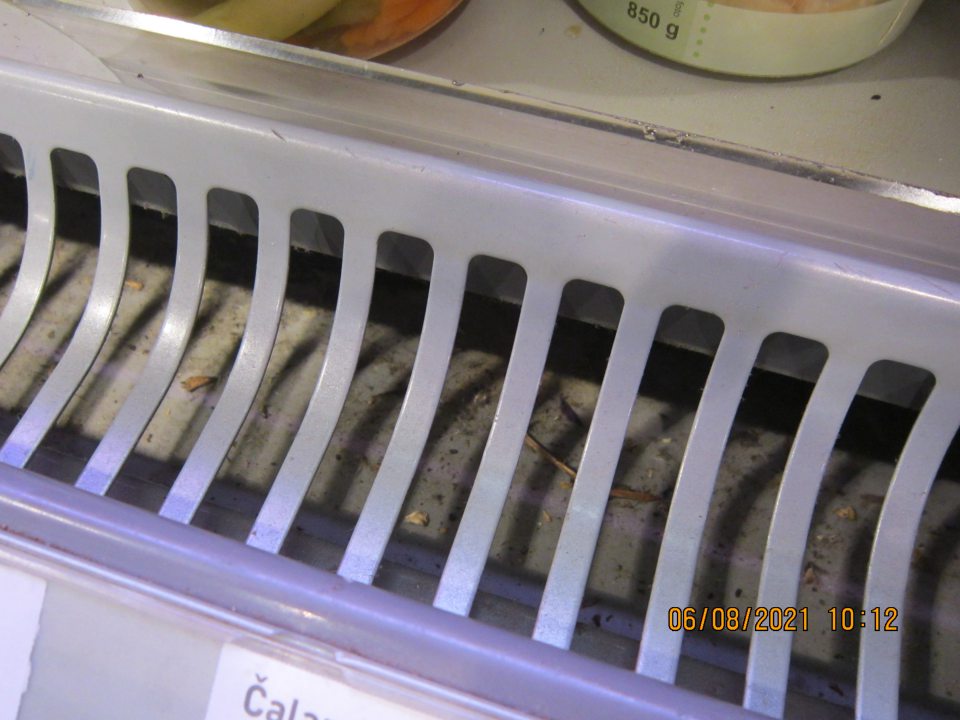 Nevyhovujúca hygiena chladiarenského zariadenia na uchovávanie balenej chladenej zeleniny, ovocných a zeleninových štiav a kvasenej zeleniny – prach, zaschnutá špina a organické nečistoty pod mriežkou zariadenia.