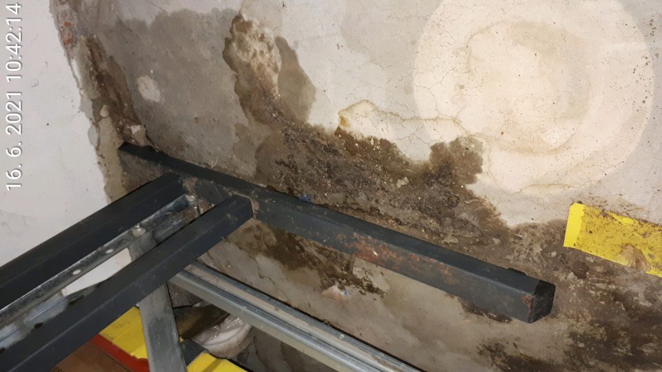 Zatečenie a poškodenie steny pod stolíkom v suchom sklade potravín.