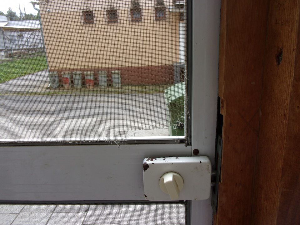 Poškodená sieťka proti hmyzu na dverách príjmu mäsových výrobkov.