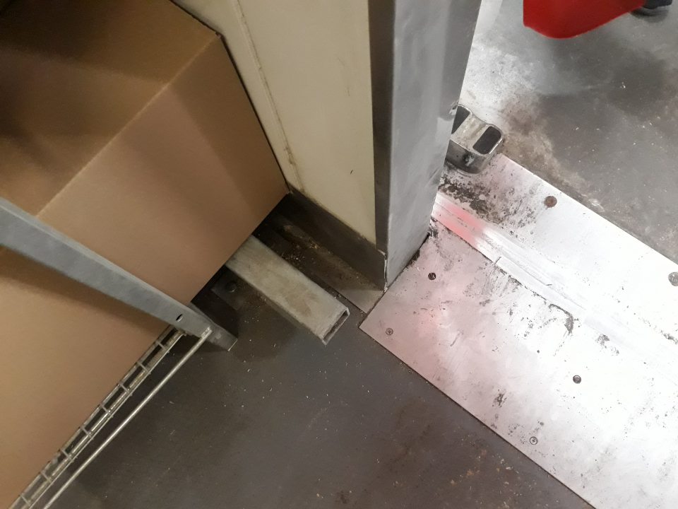 Znečistená podlaha v rohoch zasúvacích dverí do chladiaceho a mraziaceho boxu v sklade.