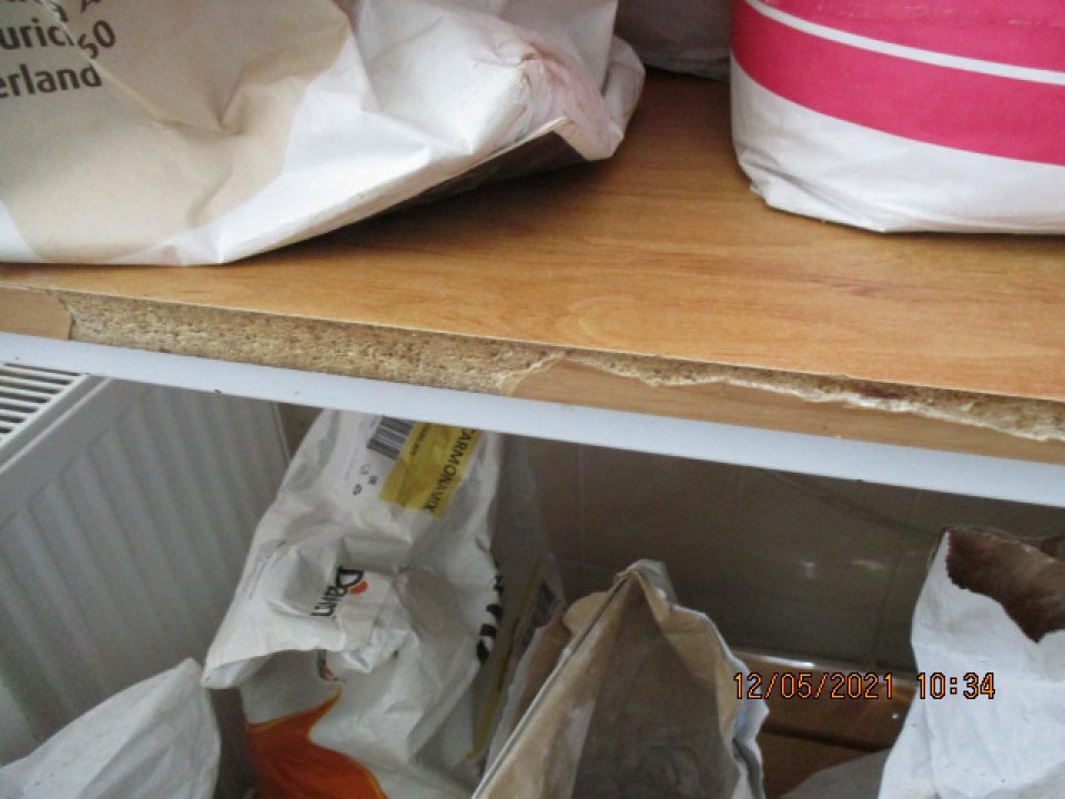 V suchom sklade kovový regál s uloženými surovinami poškodené olupujúce sa hrany police na viacerých miestach