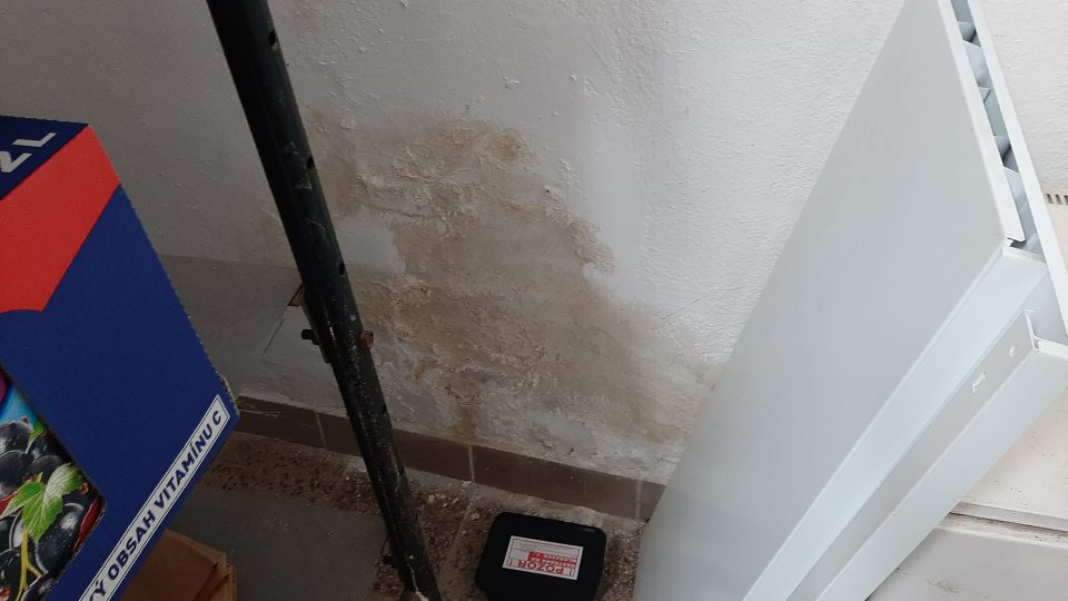 Poškodená a zvlhnutá stena v suchom sklade potravín v blízkosti regálu s s trvanlivým mliekom a džúsmi, opadaná omietka, stena nie je celistvá a ťažko čistiteľná.