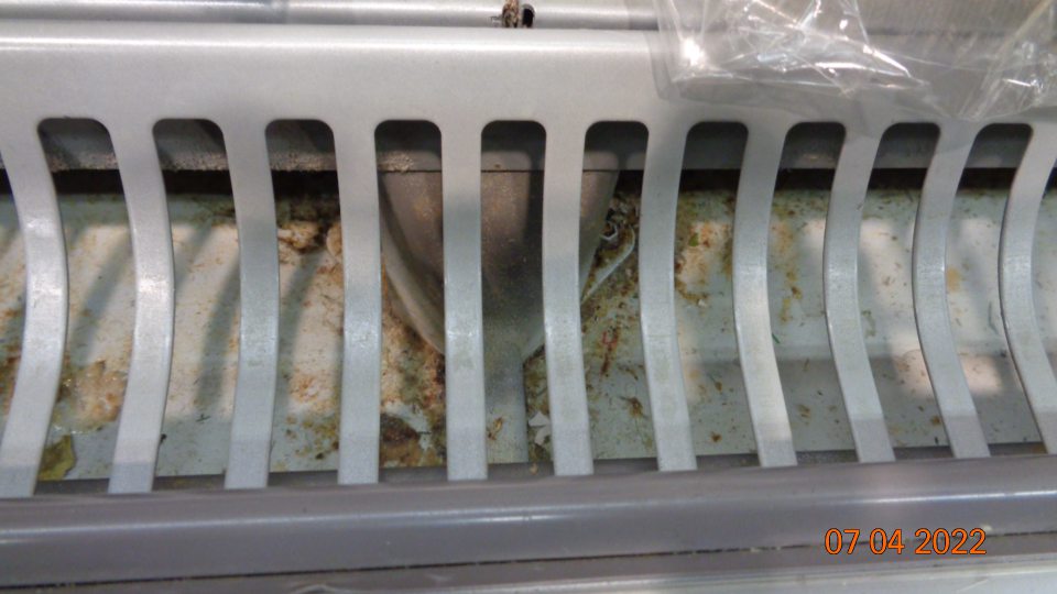 Priestor pod mriežkou na vitríne určenej na predaj mlieka a mliečnych výrobkov hrubo znečistený.