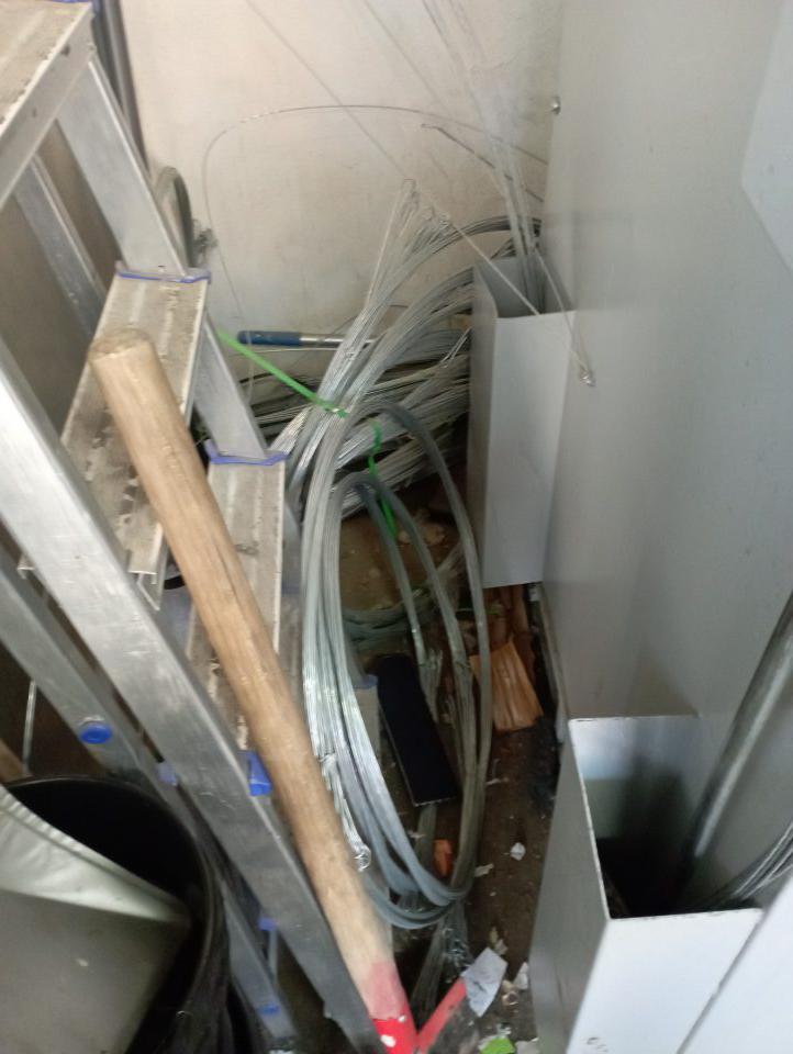 V zázemí predajne vedľa lisu sú uložené predmety nesúvisiace s činnosťou ( hliníkový rebrík, káble, lopata).