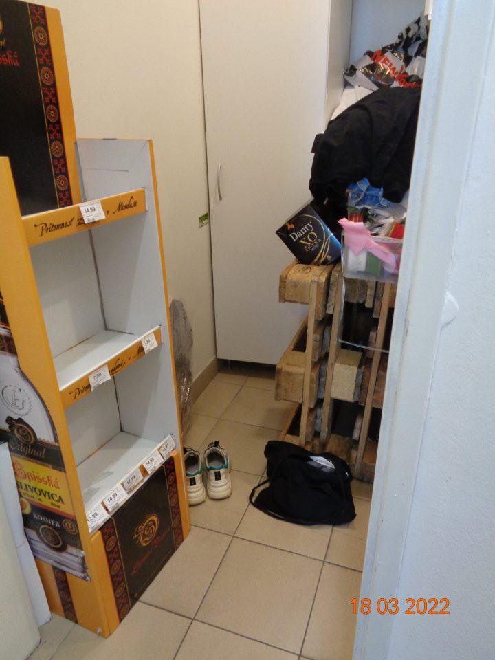 V priestoroch šatne zamestnancov skladované tri drevené palety, obalový materiál, darčekové tašky a stuhy na balenie, mimo skrine je uložené šatstvo, obuv a kabelka predavačky. 