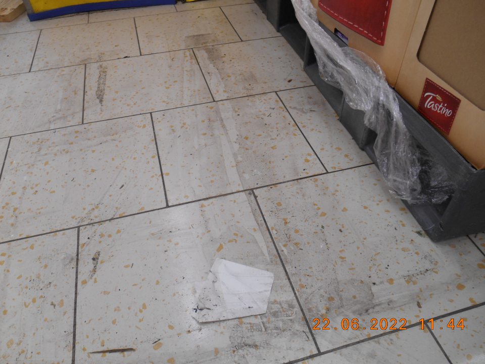 Znečistená podlaha v predajnej časti prevádzky zaschnutou čiernou špinou, prachom a kúskami papiera.