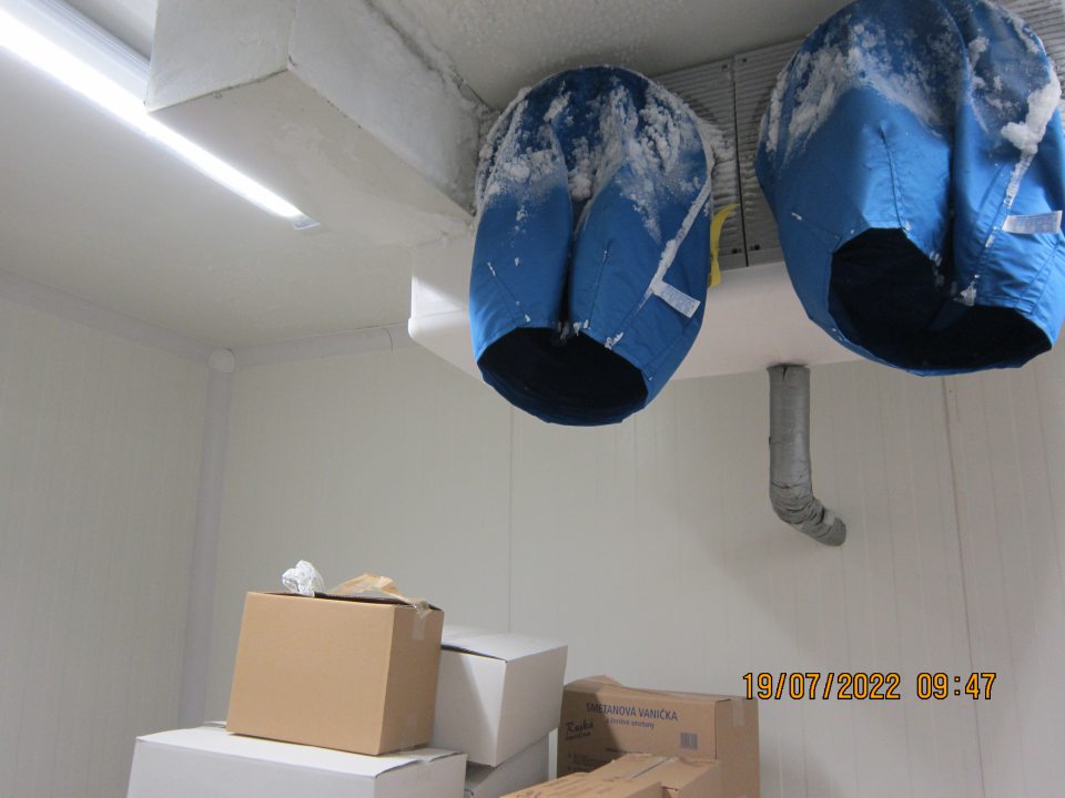 Nadmerná námraza zistená na mraziacej jednotke v mraziacom boxe TIKO v skladovacej časti prevádzky, pod ktorou sú uložené kartónové krabice s mrazenými krémami a nanukmi.