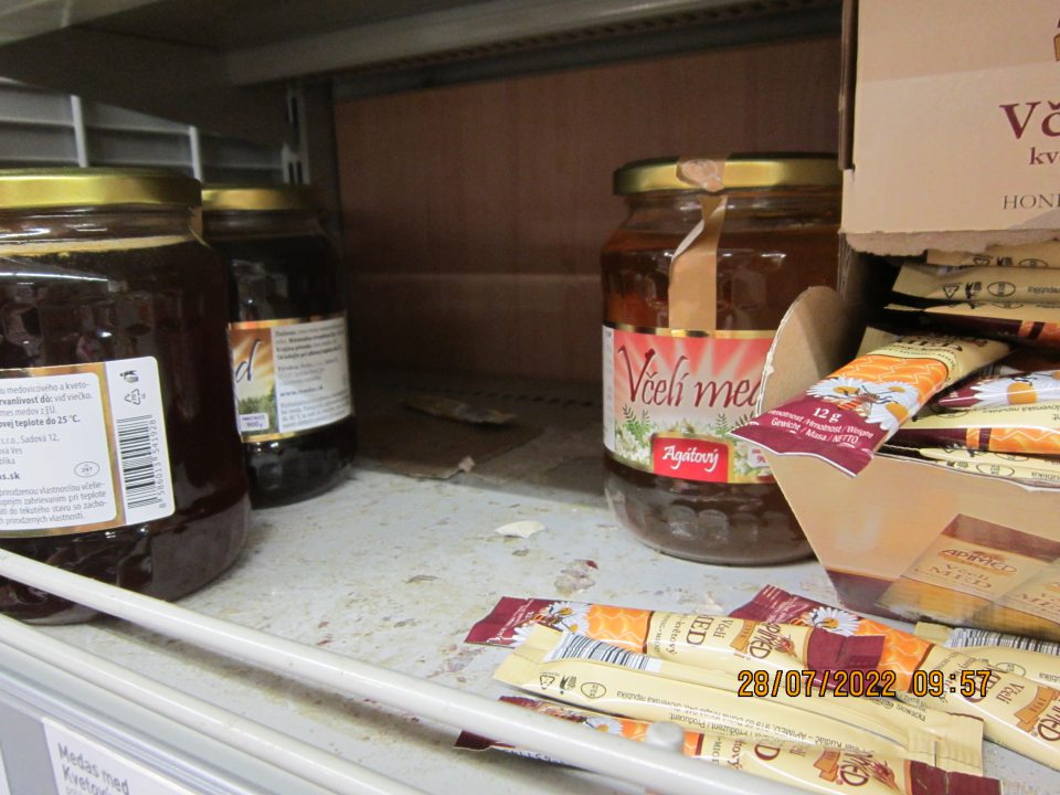 Znečistené regále na predajnej  ploche na uchovávanie včelieho medu – zaschnuté nečistoty z vytečeného obsahu z daných výrobkov a kúsky prilepeného kartóna na regáloch.