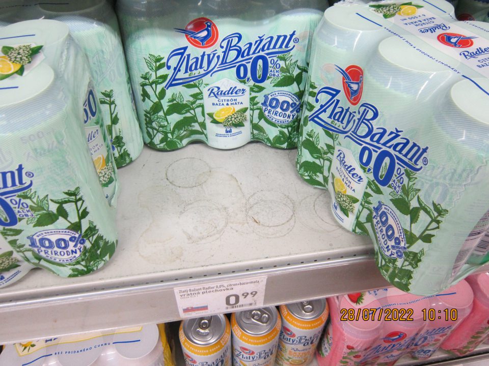 Znečistené regále na predajnej na ploche na uchovávanie pív Radler v plechovkách – zaschnuté nečistoty z vytečeného obsahu z daných výrobkov. 