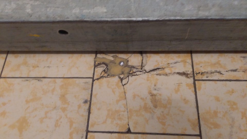 Lokálne porušená celistvosť podlahy v zázemí predajne na viacerých miestach pred chladiacim zariadením na mliečne výrobky.