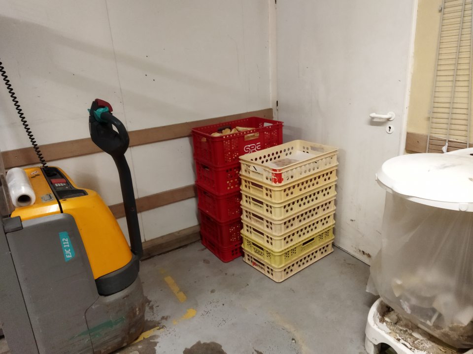 Nebalené pekárske výrobky skladované v blízkosti skladovania komunálneho odpadu a paletového vozíka.