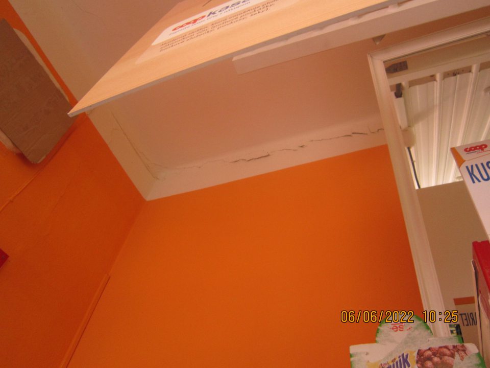 Necelistvá stena poškodená prasklinami v predajni nad regálom s tabakovými výrobkami a alkoholom  