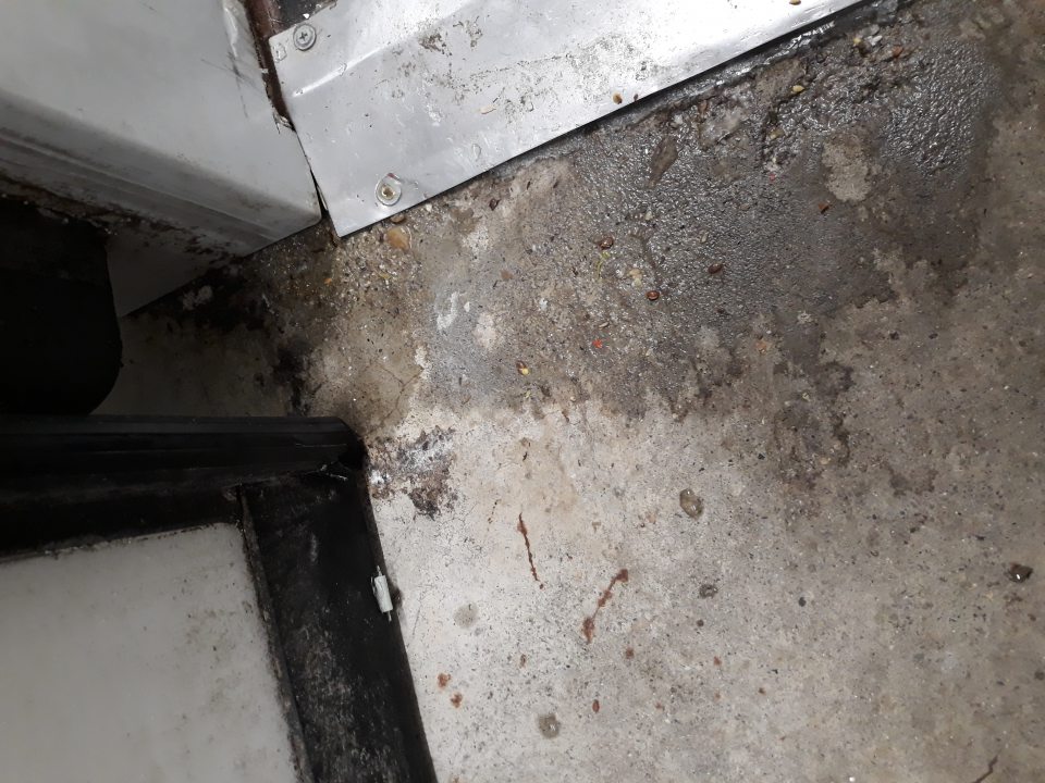 Podlaha pred dverami mraziaceho skladu pečiva silne znečistená prachom, zaschnutou tekutinou a mechanickými nečistotami.