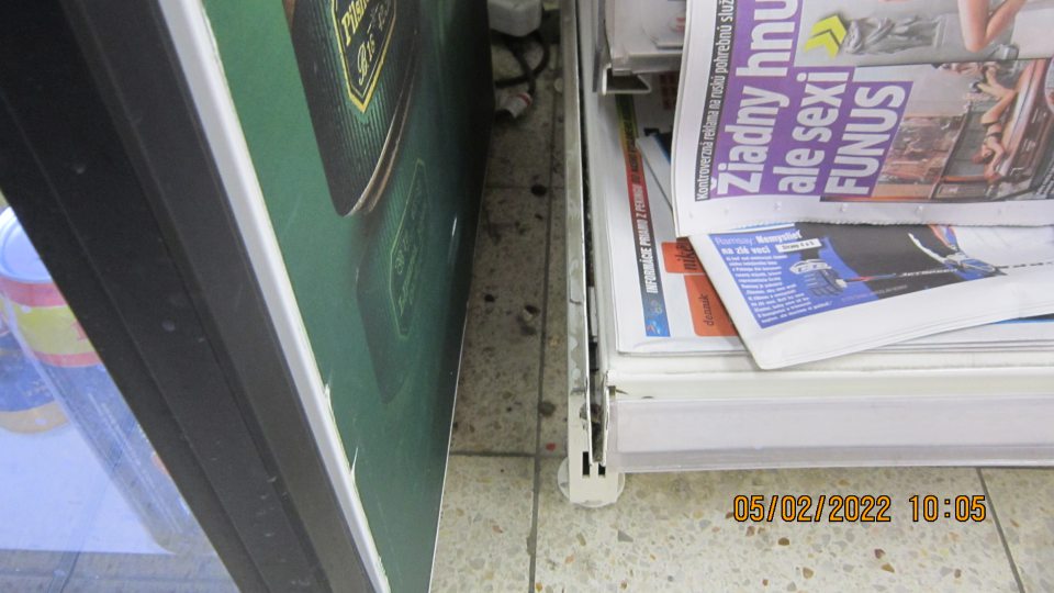 Podlaha na predajnej ploche medzi chladiacim zariadením  na vystavovanie a predaj piva v plechovke a regálom na predaj novín a časopisov silne znečistená prachom a napadanými nečistotami.