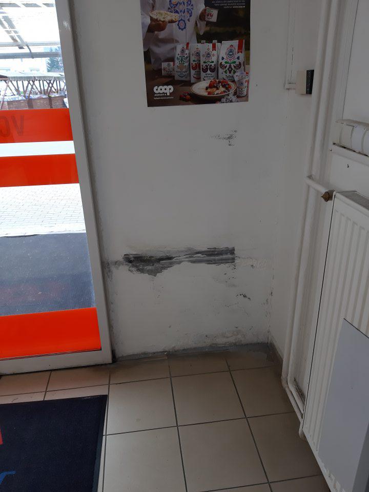Stena v okolí vstupných dverí do predajne je v spodnej časti poškodená a znečistená. 