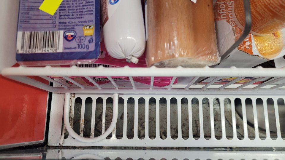 Znečistené chladiace zariadenie mliečnych výrobkov na predajnej ploche nánosom špiny a prachu.
