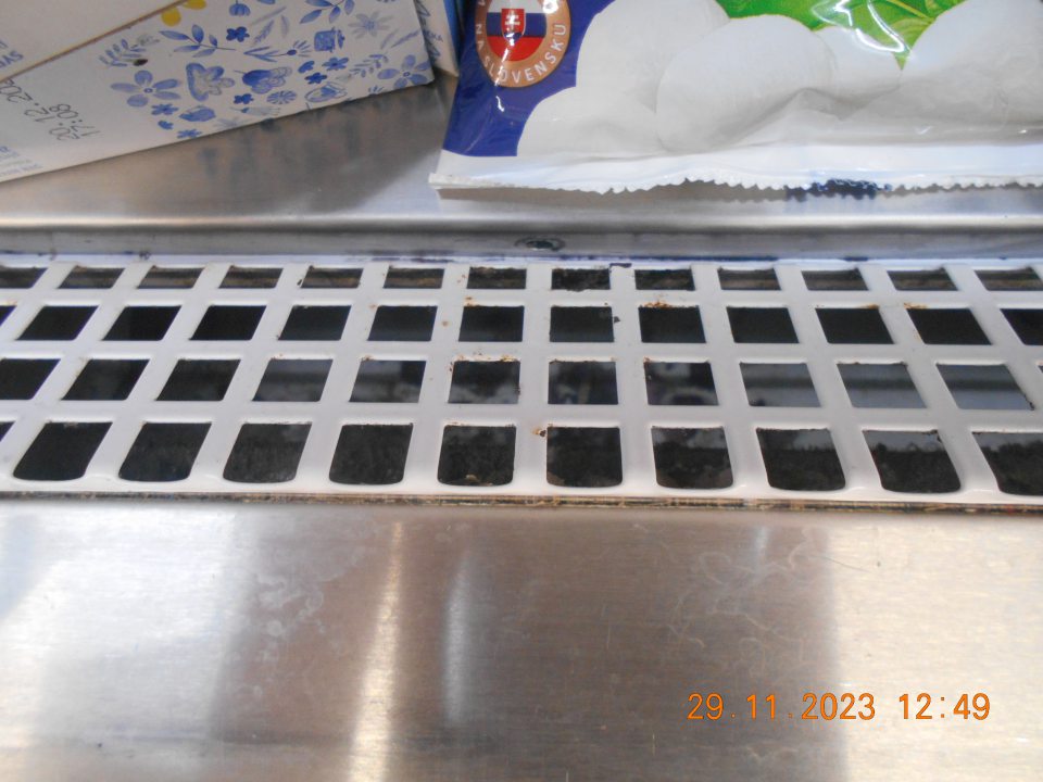 znečistený priestor chladiaceho zariadenia s uchovávanými mliečnymi výrobkami (majonézy, jogurty) pod kovovou mriežkou starými nánosmi (prach, zaschnutý vytečený obsah)