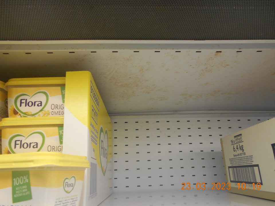 Zistená znsčistená chladiarenská vitrína s uchovávanými mliečnymi výrobkami nálepmi staršieho dáta, a to na spodnom regáli a v stropnej časti. 