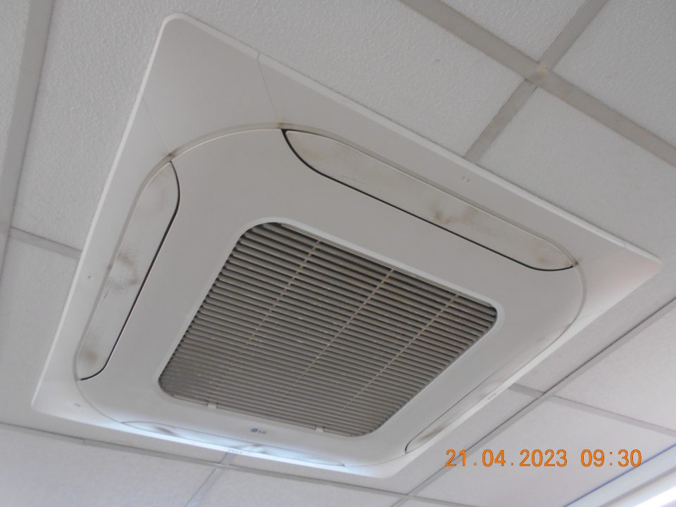 Zistená silne znečistená stropná klimatizačná jednotka nad regálmi s balenými potravinami na predajnej ploche.
