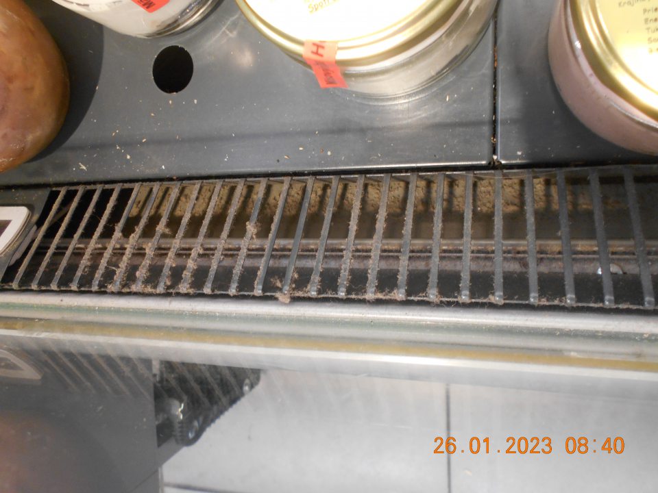 Znečistený priestor pod mriežkou a samotná mriežka v chladiarenskom zariadení s vystavovanými rybacími výrobkami a mäsovými konzervami. 