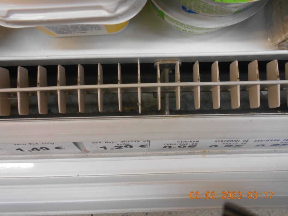 Znečistená chladiarenská vitrína s uchovávanými mliečnymi výrobkami v ťažko dostupných miestach - pod mriežkou. 