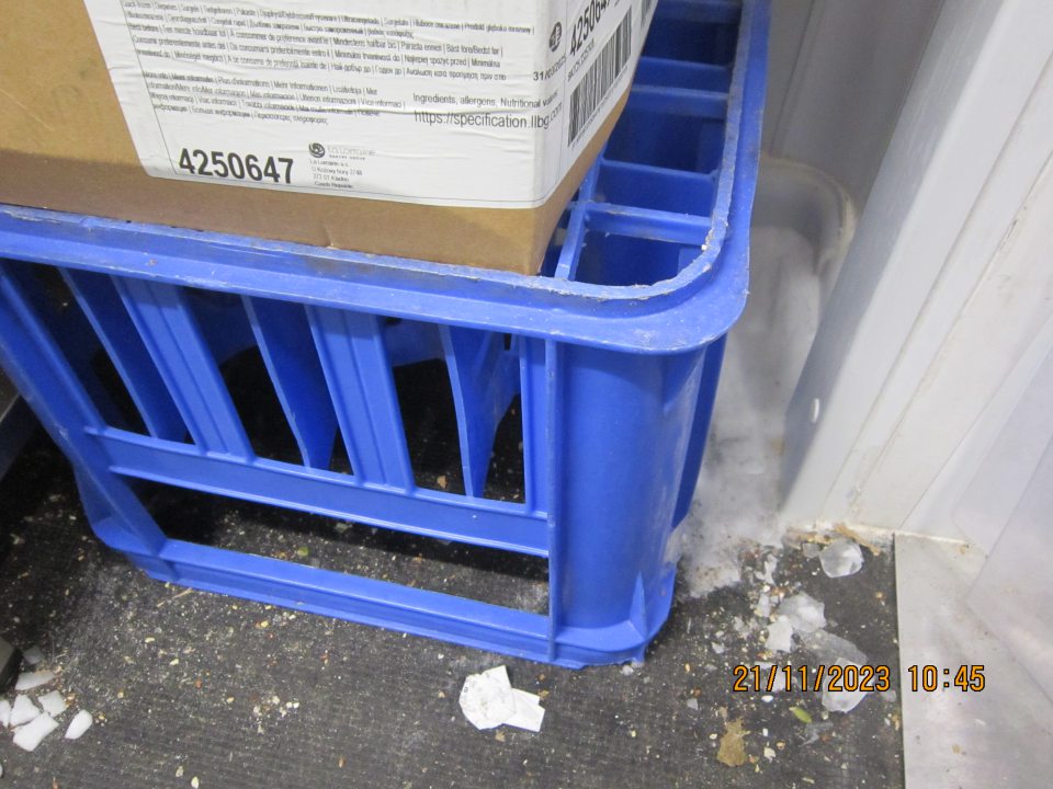 Veľké množstvo organických nečistôt (zbytky mrazených pekárskych výrobkov, semiačok z posypu), papieriky a vrstva ľadu v rohu mraziarenského skladu v zázemí prevádzky.